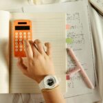A student calculates math equations using an orange calculator and notebook for study.