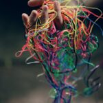 A hand holding a tangle of colorful rubber bands symbolizing chaos and creativity.