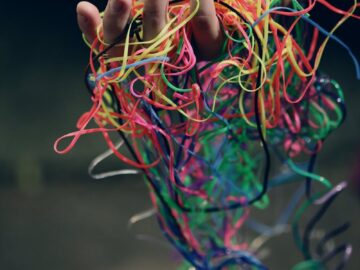 A hand holding a tangle of colorful rubber bands symbolizing chaos and creativity.