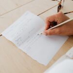 Close-up of hand writing math equations on graph paper, indicating study and learning.