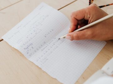 Close-up of hand writing math equations on graph paper, indicating study and learning.