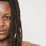 Crop young feminine African American male with braided hairstyle looking at camera on white background
