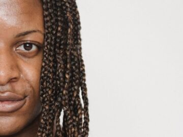 Crop young feminine African American male with braided hairstyle looking at camera on white background