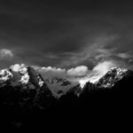 Stunning black and white photo of snow-capped mountains under a dramatic sky.