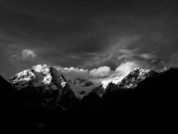 Stunning black and white photo of snow-capped mountains under a dramatic sky.