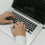 Close-up of hands typing on a laptop with a USB device on a white background. Ideal for tech and cybersecurity themes.