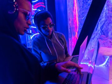 Two individuals working on laptops in a neon-lit setting, emphasizing technology and teamwork.