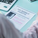 From above back view of crop anonymous female with marker and paper sheet with illustration studying in daylight