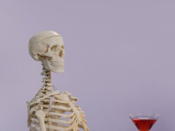 Skeleton model with a cocktail glass on a purple background, playful and intriguing vibe.