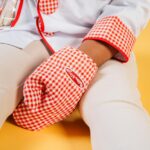 Child wearing a checkered chef outfit and oven glove on a vibrant yellow background.