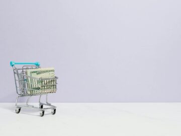 Shopping cart filled with cash on a plain background, ideal for finance and retail themes.