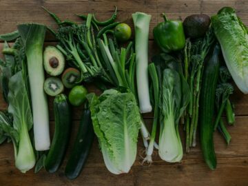 High-angle view of assorted fresh green vegetables arranged on a wooden table.