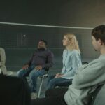 Diverse group of adults in a supportive indoor discussion setting. Sharing experiences.