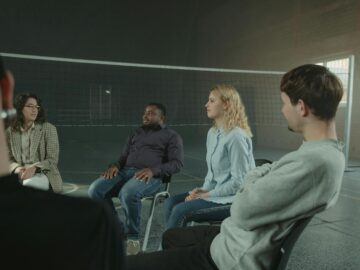 Diverse group of adults in a supportive indoor discussion setting. Sharing experiences.