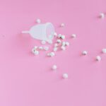 White menstrual cup with flowers on a pink background symbolizing femininity and hygiene.