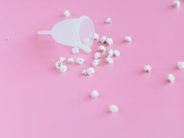 White menstrual cup with flowers on a pink background symbolizing femininity and hygiene.