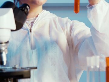 A female scientist in protective gear analyzing a test tube in a laboratory setting.