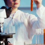 A female scientist in protective gear analyzing a test tube in a laboratory setting.