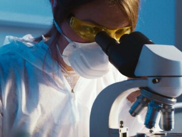 A female scientist examines a sample using a microscope in a laboratory setting.