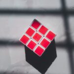 A geometric cube with red squares on a white surface and shadow patterns.