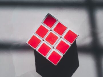 A geometric cube with red squares on a white surface and shadow patterns.