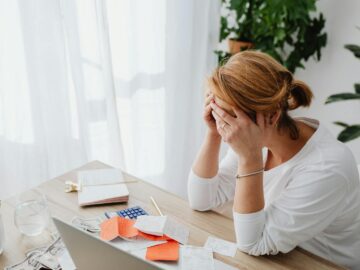 Woman stressed over financial receipts at a desk, dealing with expenses and calculations.