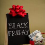 A chalkboard sign with Black Friday written on it and a small shopping cart with dollar bills, ideal for sales promotions.
