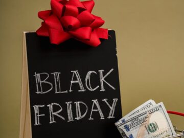 A chalkboard sign with Black Friday written on it and a small shopping cart with dollar bills, ideal for sales promotions.