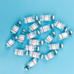 Top view of multiple Covid-19 vaccine vials on a blue background emphasizing vaccination effort.