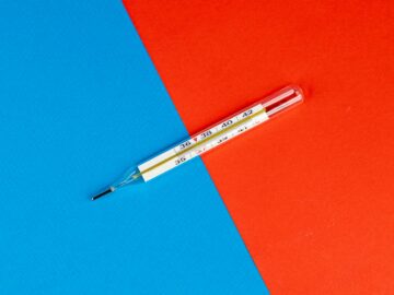 Glass thermometer on a vibrant red and blue background, symbolizing health and temperature measurement.