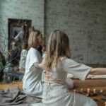 Two women in white dresses meditating indoors with candles and serene ambiance.