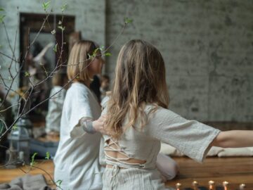 Two women in white dresses meditating indoors with candles and serene ambiance.