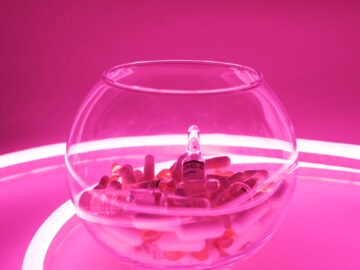 Glass bowl full of pills and vaccine for coronavirus in bright neon light
