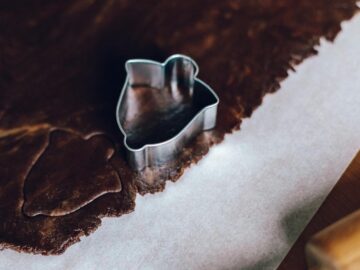 Close-up of uncooked chocolate dough with a stainless steel cookie cutter on wax paper.