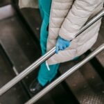 Unrecognizable female wearing medical uniform latex gloves and coat going down on metal stairs leaning on metal handrails
