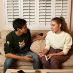 A couple sitting on a couch discussing pregnancy test results in a cozy living room.