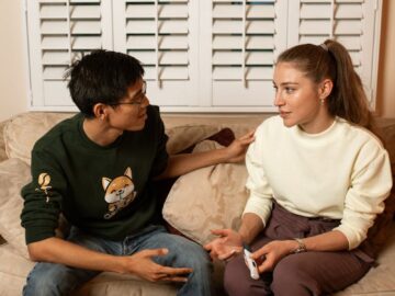A couple sitting on a couch discussing pregnancy test results in a cozy living room.