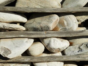 A vertical arrangement of smooth stones secured by wooden slats in natural light.