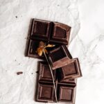 A flat lay of dark chocolate pieces with a dried flower elegantly placed, emphasizing artisanal confectionery.