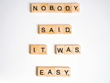 Close-up of wooden Scrabble tiles spelling 'nobody said it was easy' on a white background.
