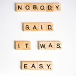 Close-up of wooden Scrabble tiles spelling 'nobody said it was easy' on a white background.