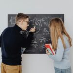 Two students working together on trigonometric equations on a blackboard, enhancing learning.