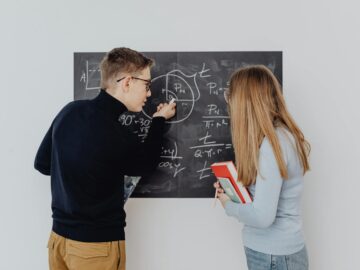 Two students working together on trigonometric equations on a blackboard, enhancing learning.