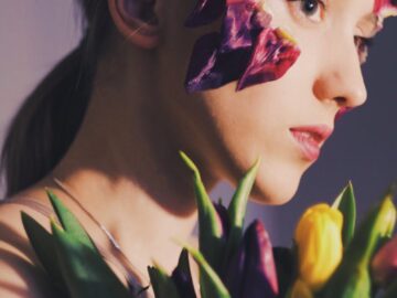 A unique side-profile portrait of a woman with floral art on face, holding tulips.