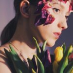 A unique side-profile portrait of a woman with floral art on face, holding tulips.