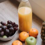 High angle of plastic bottle with juice bowl with red grapes and some mandarins and green apple on table