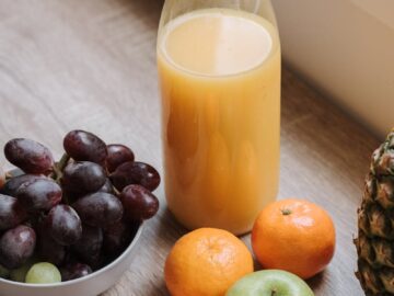 High angle of plastic bottle with juice bowl with red grapes and some mandarins and green apple on table