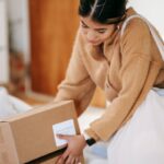 Female customer with shopping bag getting stack of carton boxes with delivered goods at home