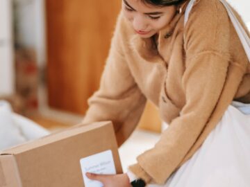 Female customer with shopping bag getting stack of carton boxes with delivered goods at home