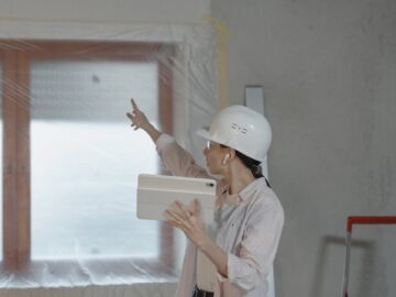 Woman in hard hat using tablet to oversee home renovation in a partially completed room.